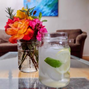 glass of water with slices of lemon and a small vase of garden flowers