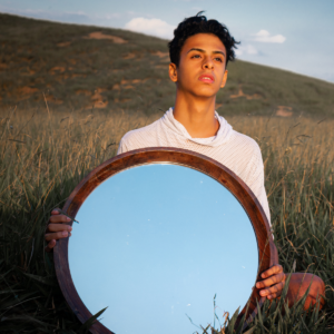 young man holding a mirror in a field
